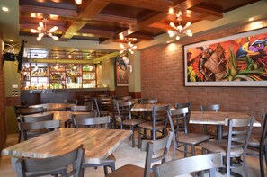 Un restaurante con paredes de ladrillo, mesas y sillas de madera. Hay una zona de bar con estantes llenos de botellas y un mural en la pared.