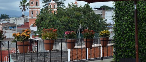 A balcony with potted plants, a view of a church, and a red umbrella.