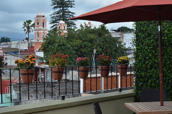 A balcony with potted plants, a view of a church, and a red umbrella.