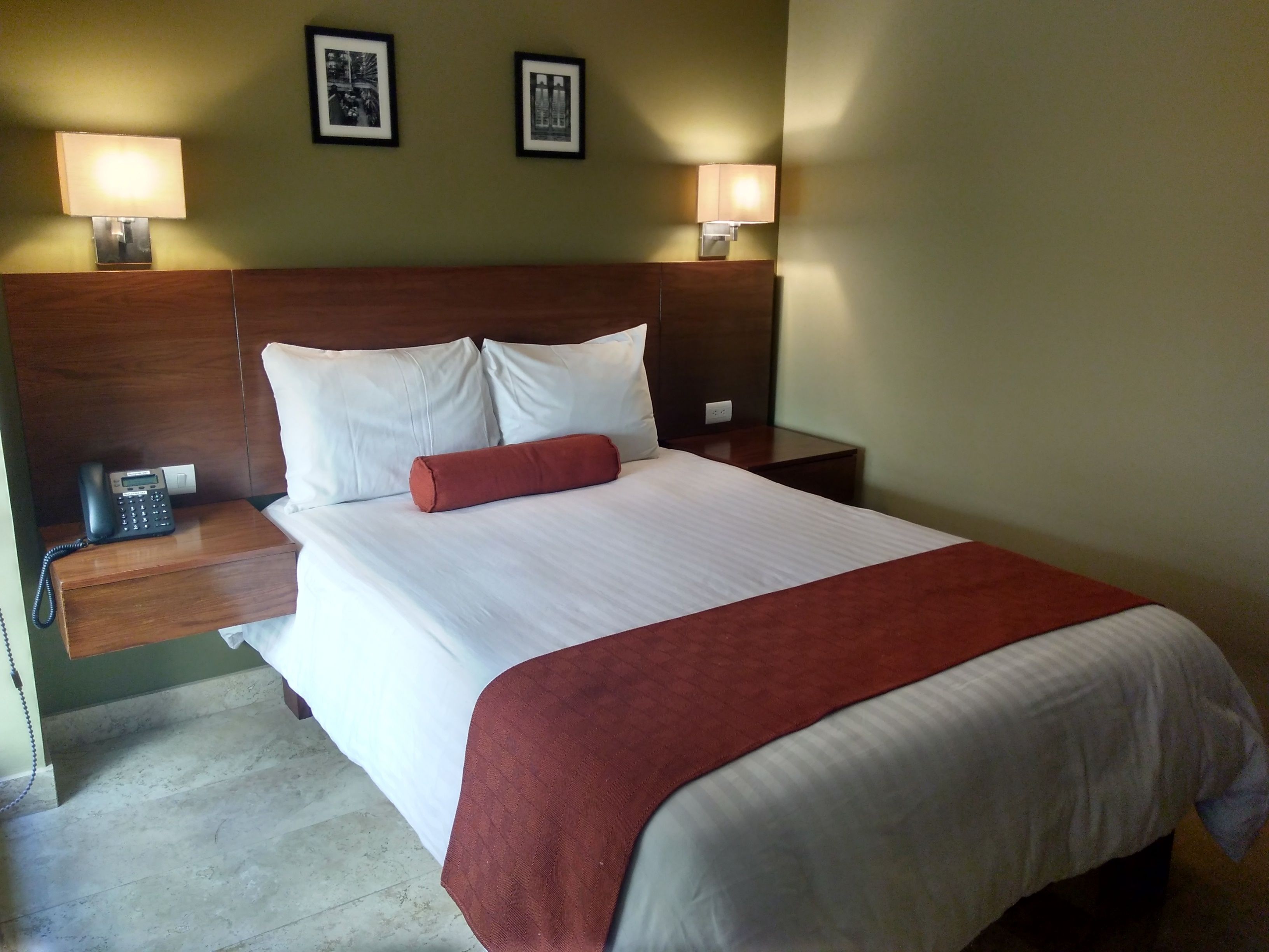 A hotel room with a large bed, two bedside lamps, a telephone, and two framed pictures on the wall.