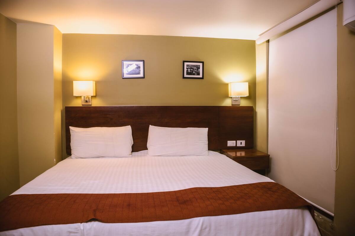 A hotel room with a large bed, two bedside lamps, and two framed pictures on the wall.