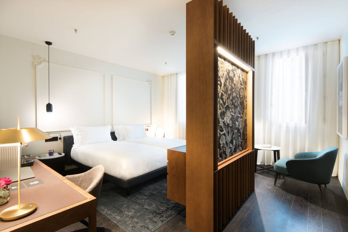 Una habitació d'hotel amb un llit gran, un escriptori amb una làmpada, una cadira i una taula petita.