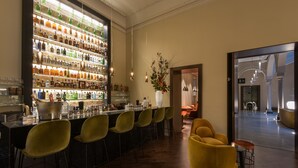 Una zona de bar con una barra larga, varios taburetes y una pared llena de botellas de licores.