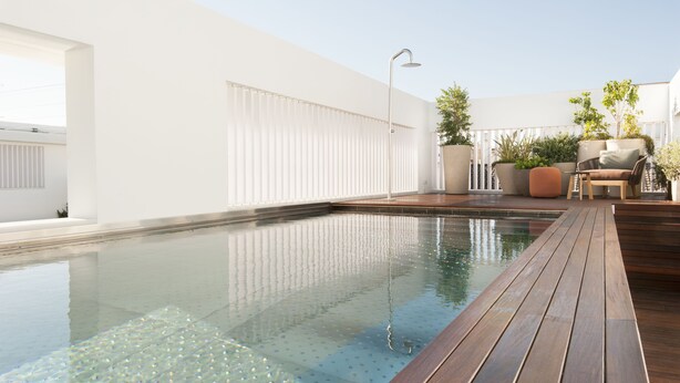 Un área de piscina moderna al aire libre con cubierta de madera, una silla de descanso y plantas en macetas.