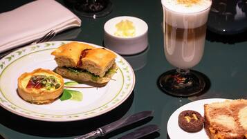 Una mesa con un sándwich, un vaso de bebida, un cuenco pequeño y un plato con un pastel.