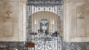 Un vestíbulo con suelo de mármol, una reja de hierro forjado y una zona de estar con mesa y sillas.