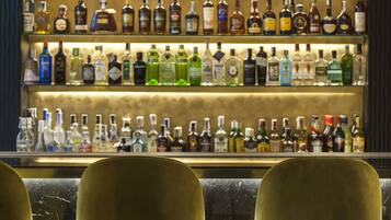 A bar with multiple shelves of liquor bottles and three gold-colored bar stools.