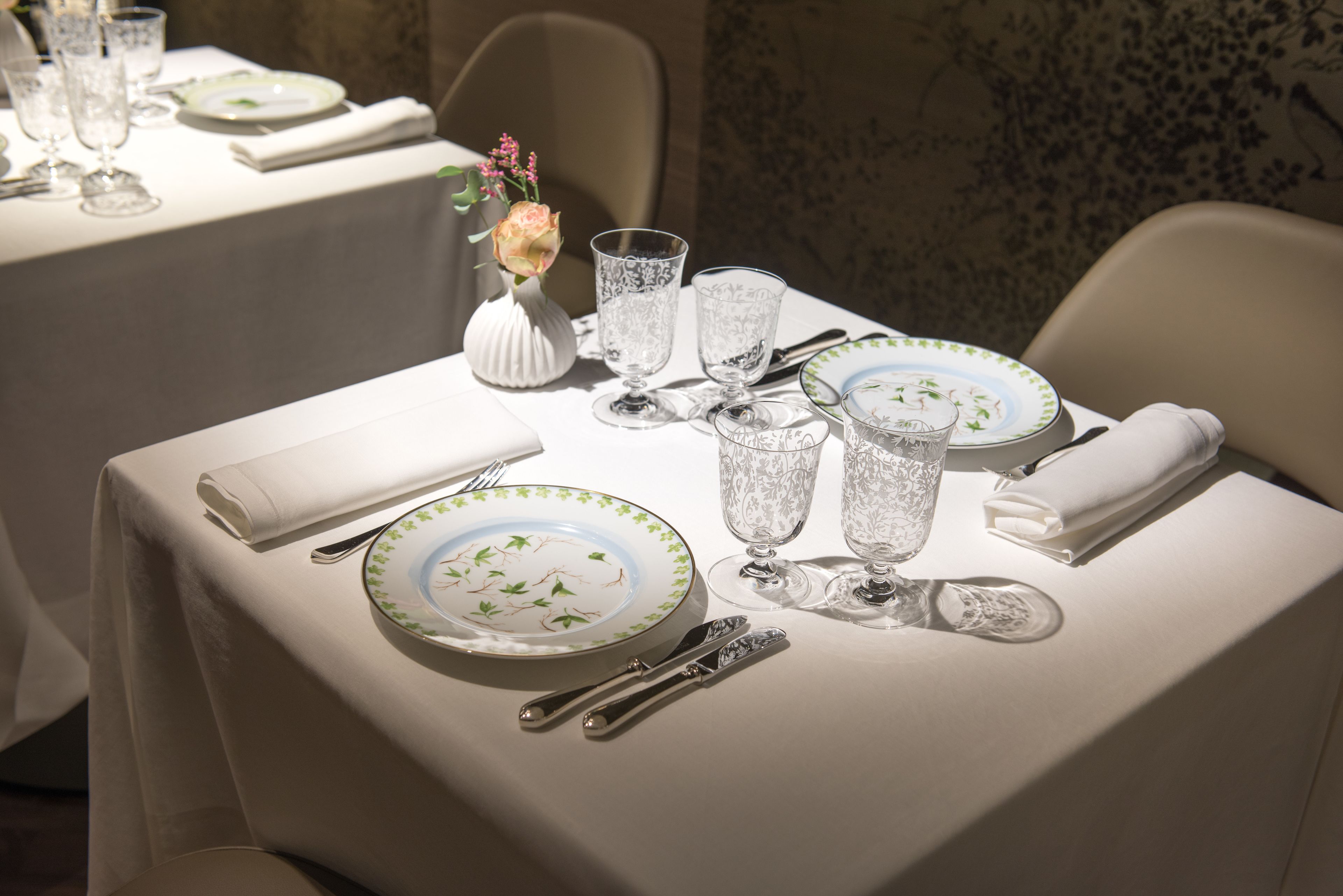 A dining table set with plates, glasses, cutlery, and a vase with flowers.