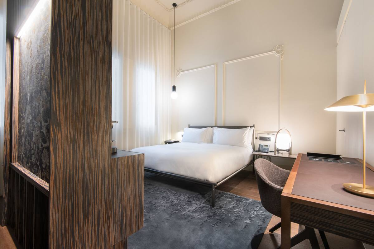 Habitació d'hotel moderna amb llit, escriptori, cadira i una finestra gran amb cortines.