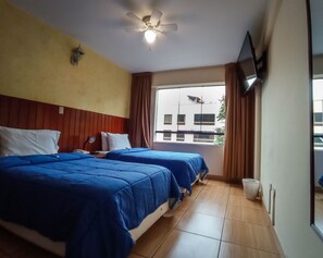 Une chambre d’hôtel avec deux lits, un ventilateur de plafond, un téléviseur fixé au mur et une fenêtre avec des rideaux.