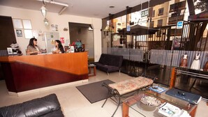 A reception area with a wooden desk, black leather sofa, and a glass coffee table. - Hotel El Farolito (Lima)