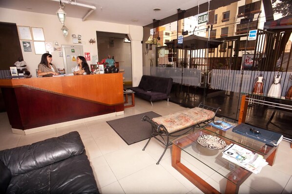 A reception area with a wooden desk, black leather sofa, and a glass coffee table. - Hotel El Farolito (Lima)