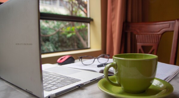 A laptop on a table with a green mug and glasses beside it.