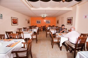 Un espace repas avec des tables et des chaises, un lustre et des œuvres d’art encadrées accrochées aux murs.