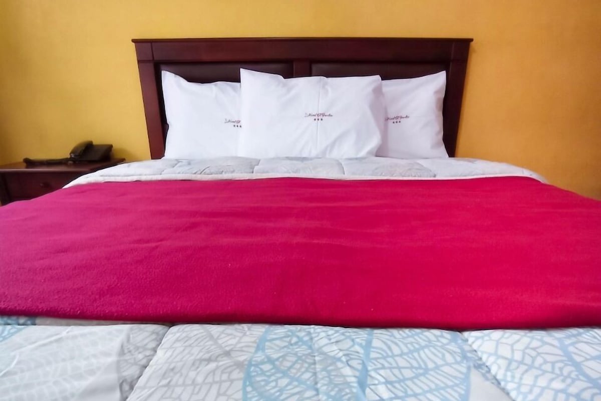 A bed with a red blanket and white pillows, a wooden headboard, and a yellow wall.