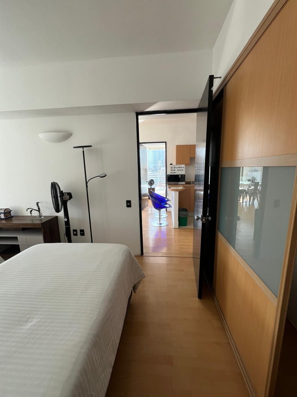Ett modernt hotellrum med en säng, ett skrivbord, en stol och ett litet kök.