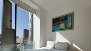 Un dormitorio moderno con una cama grande, una mesita redonda y vistas a la ciudad a través de un ventanal amplio.