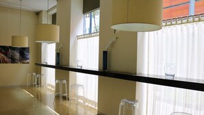Un interior moderno con una larga barra de madera oscura, taburetes de plástico transparente y un amplio ventanal con cortinas de gasa.