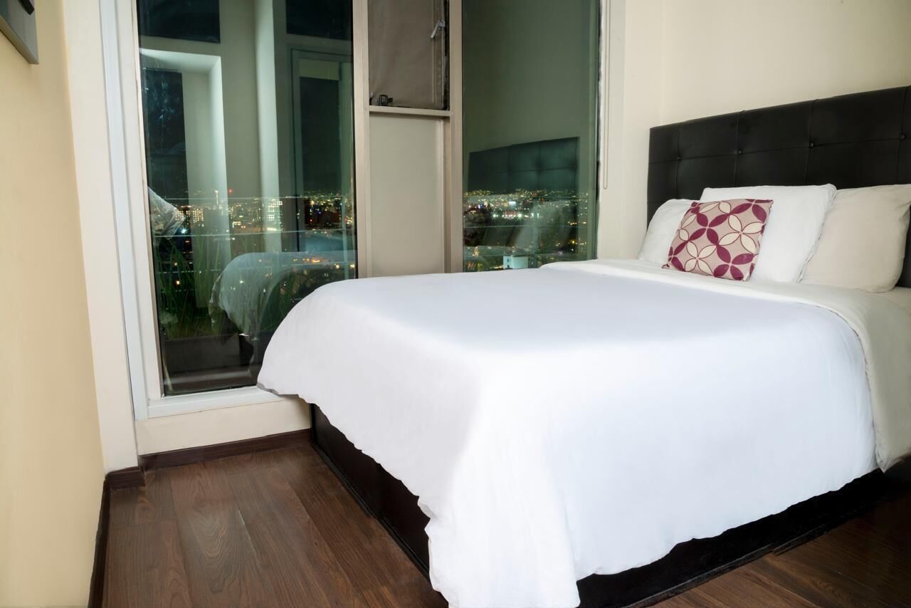 A hotel room with a large bed, a view of the city through a window, and a cityscape visible outside.