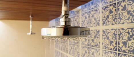 Un cabezal de ducha con agua brotando, montado en una pared de azulejos con un diseño decorativo.