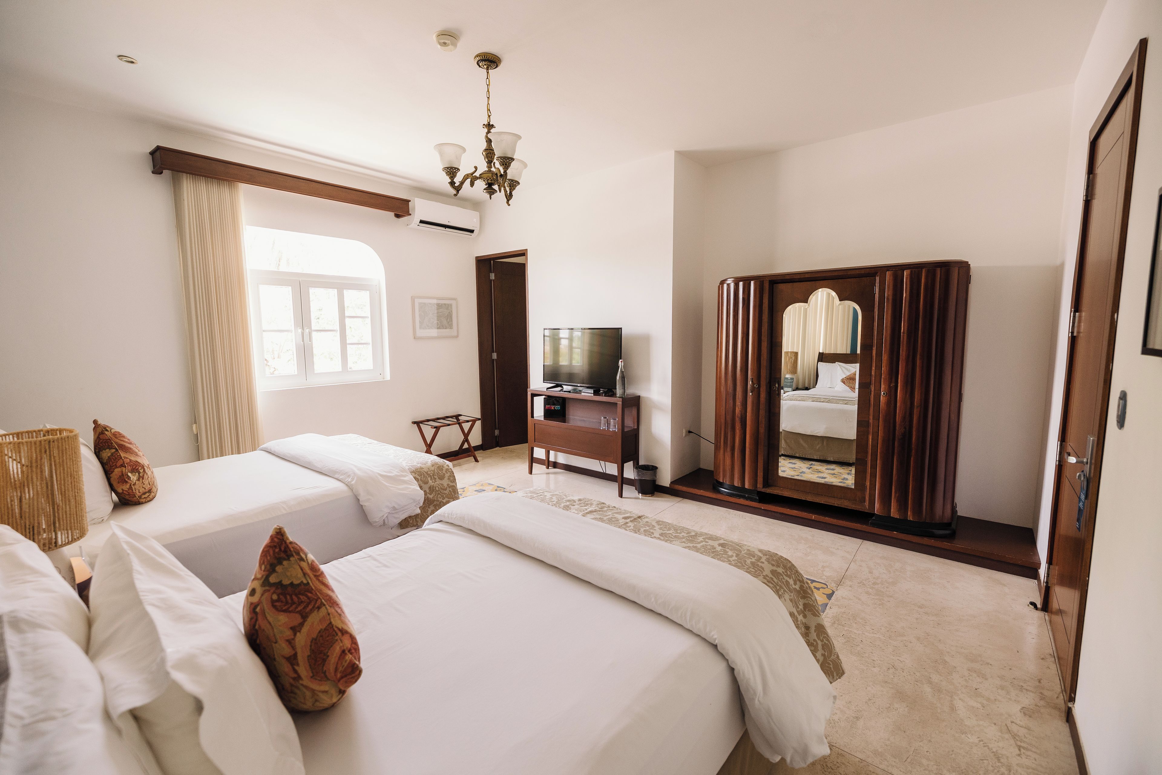 Habitación de hotel con dos camas, televisión, armario y un espejo grande.