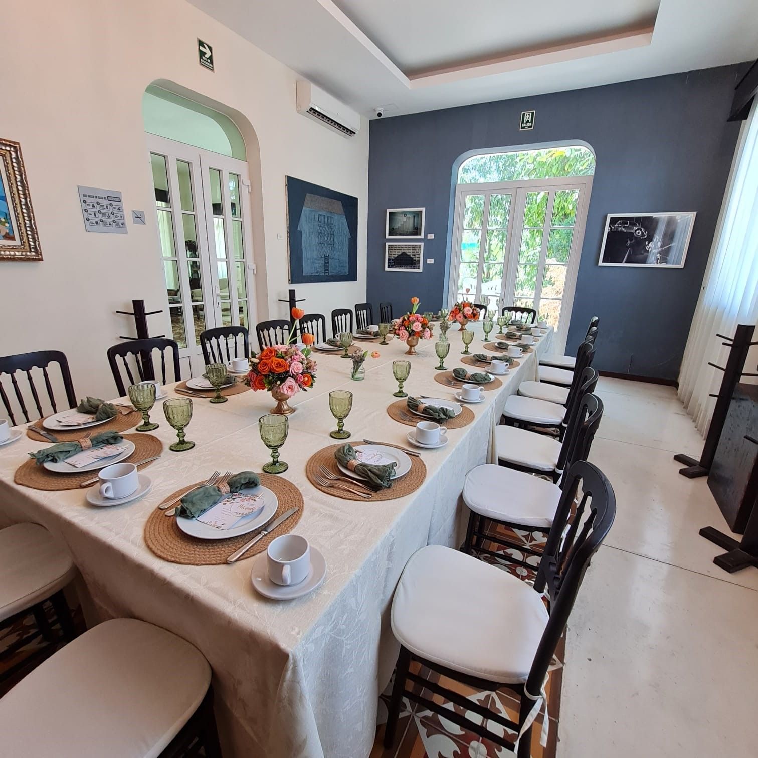 Comedor con una larga mesa dispuesta para una comida, sillas y vistas al exterior.