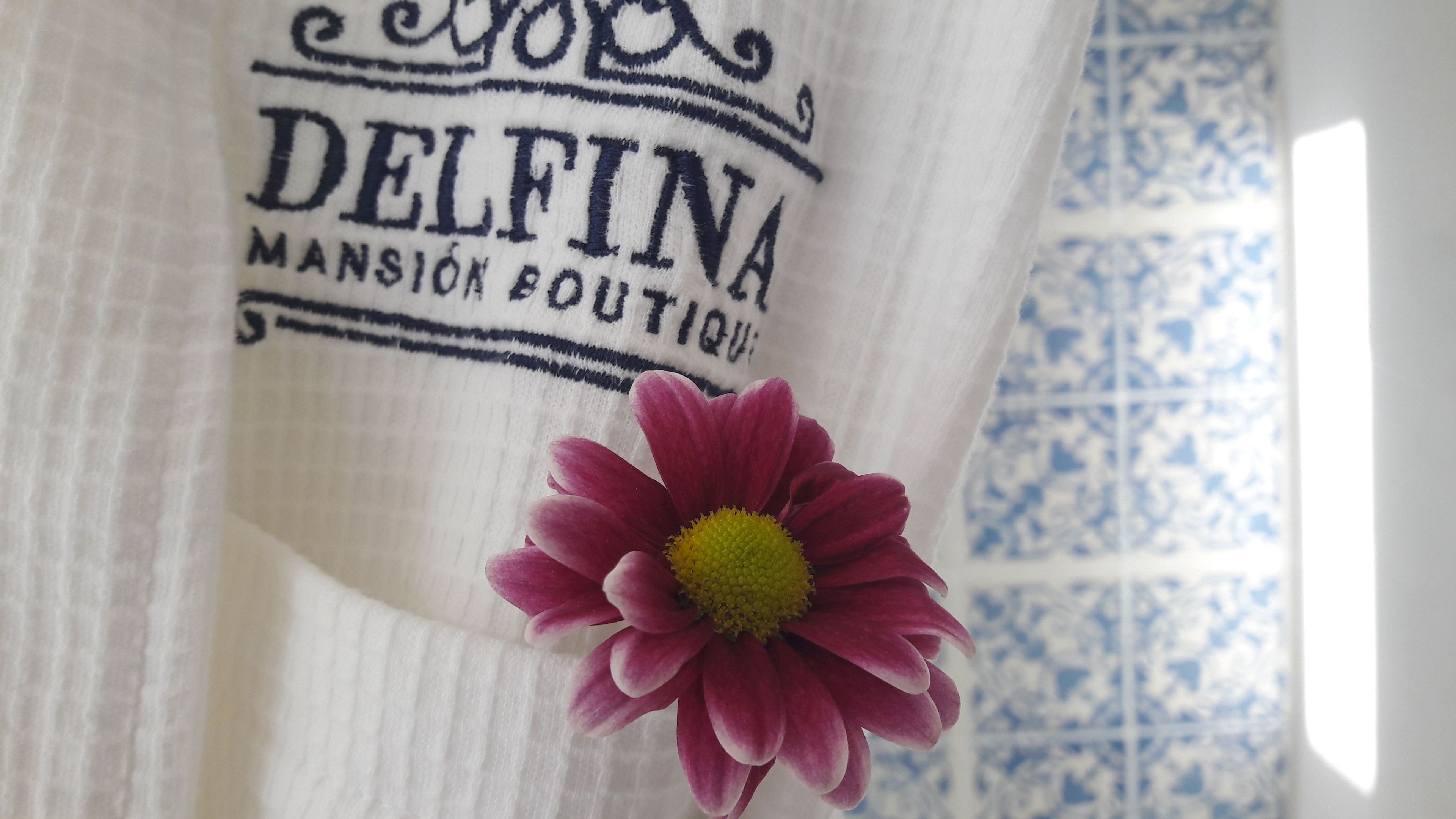 Een witte stof met geborduurd opschrift 'DELFINA MANSION BOUTIQUE'.