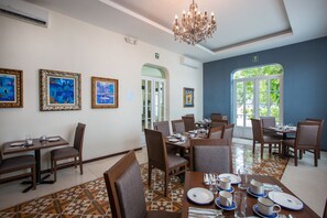 Un espace repas avec des tables dressées pour le service, des œuvres d’art encadrées aux murs et un lustre.