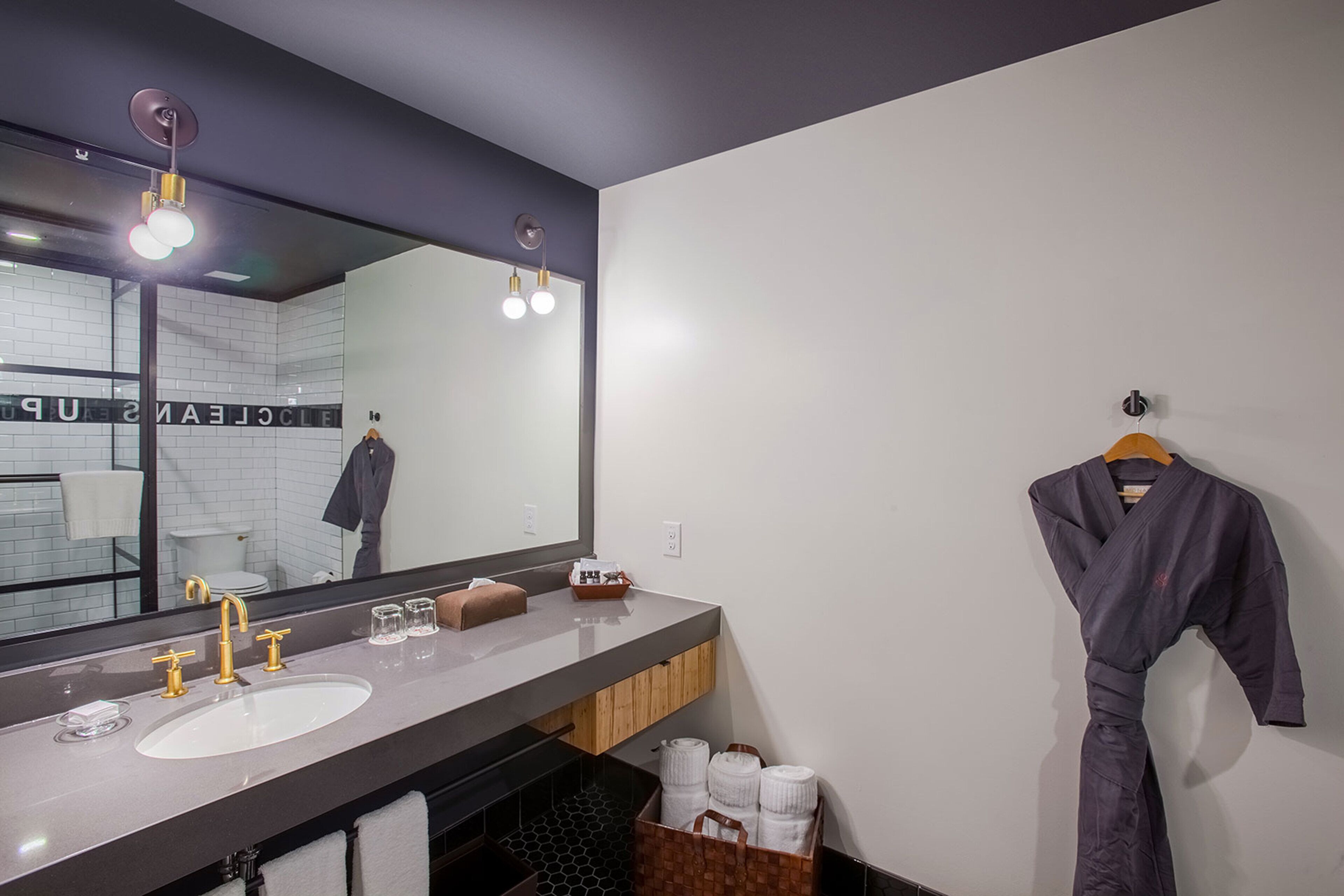 A modern bathroom with a large mirror, dual sinks, and a robe hanging on the wall.