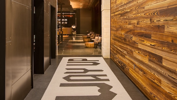 A hallway with a wooden wall, a tiled floor with directional arrows, and hanging pendant lights.
