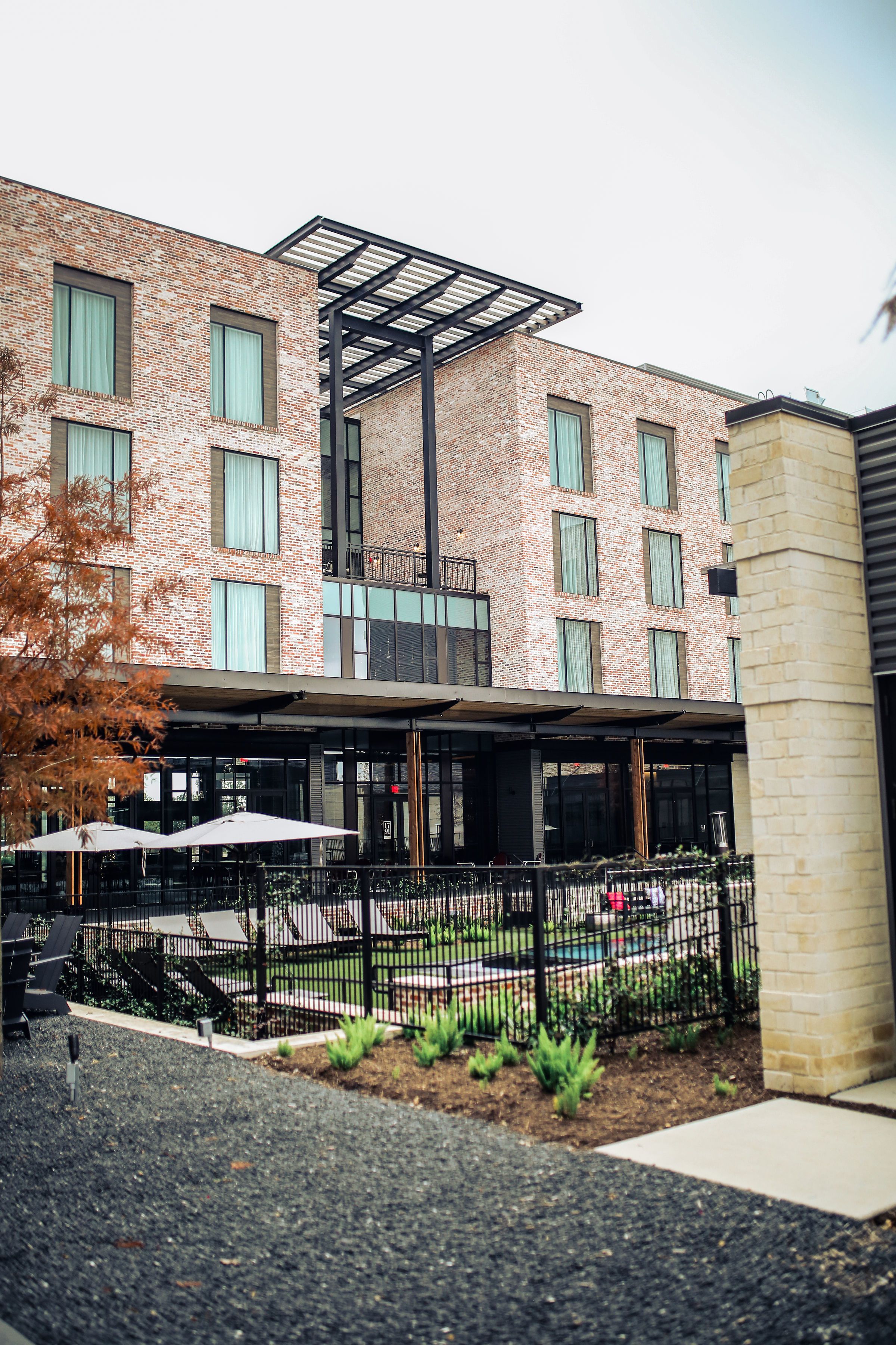 Een modern gebouw met een bakstenen gevel, grote ramen en een overdekt terras met parasols.
