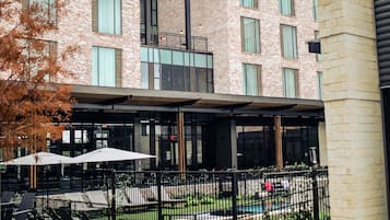 Een modern gebouw met een bakstenen gevel, grote ramen en een overdekt terras met parasols.