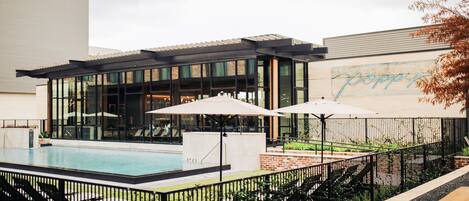Un edificio moderno con zona de piscina, sillones y sombrillas.