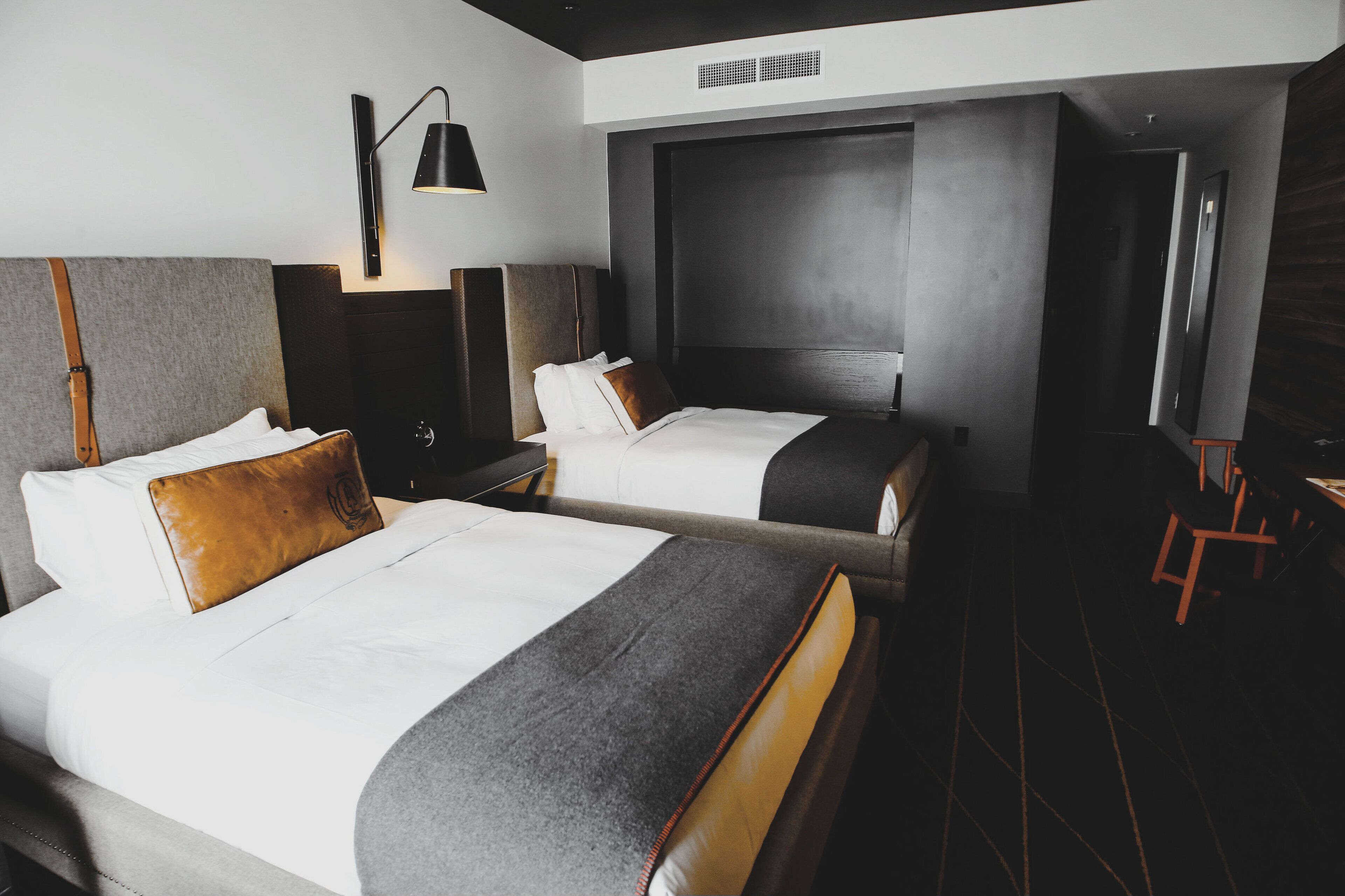 A hotel room with two beds, a desk, a chair, a lamp, and a large window.
