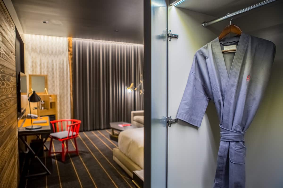 A hotel room with a bed, a desk, a chair, and a robe hanging on the door.
