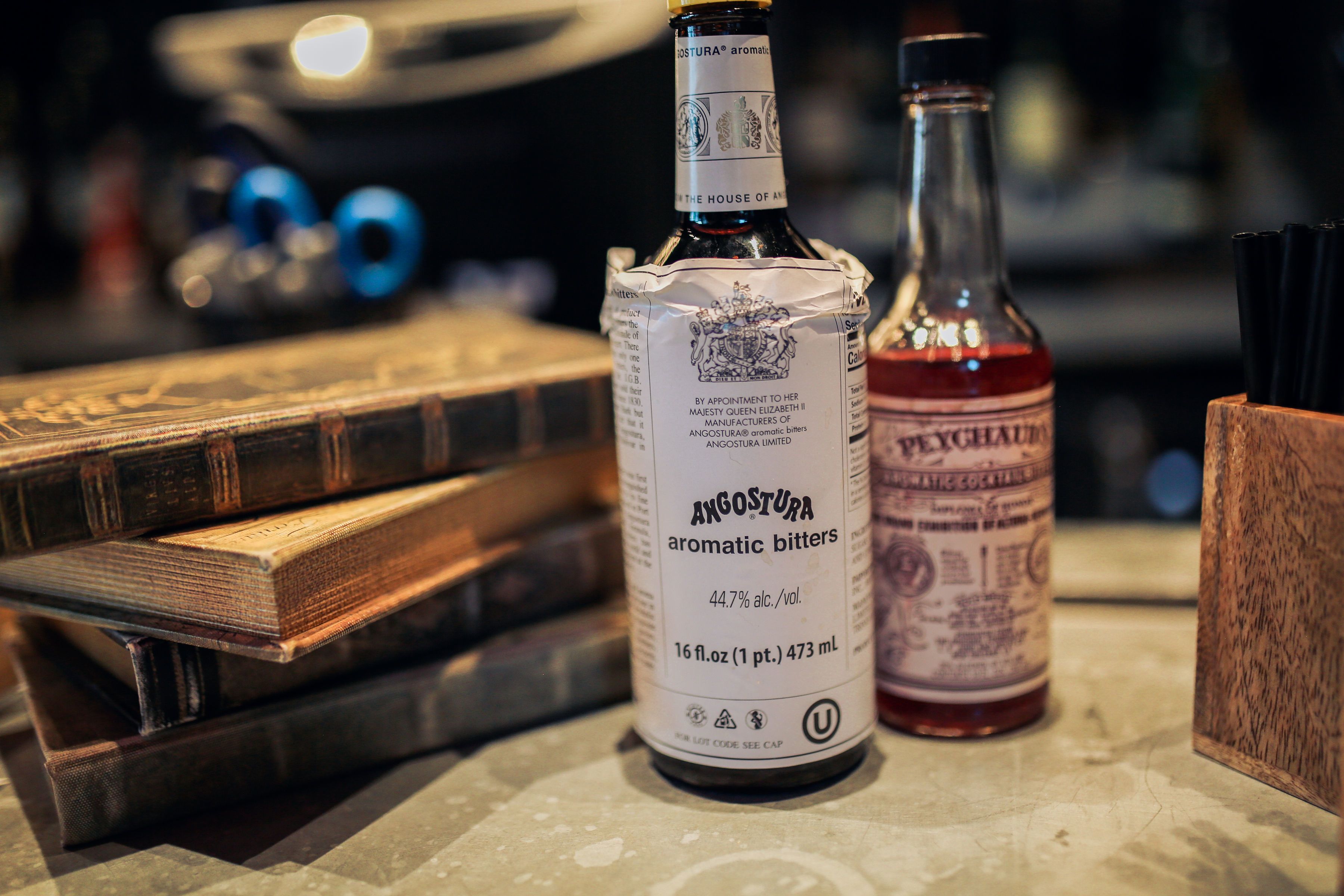 A bottle of Angostura aromatic bitters and a bottle of Peychaudan syrup on a table with books.
