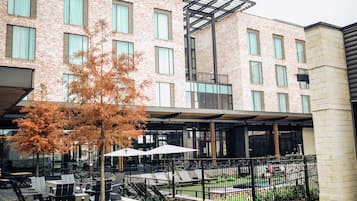 A modern building with a brick facade, outdoor seating area with tables and chairs, and a small pool.