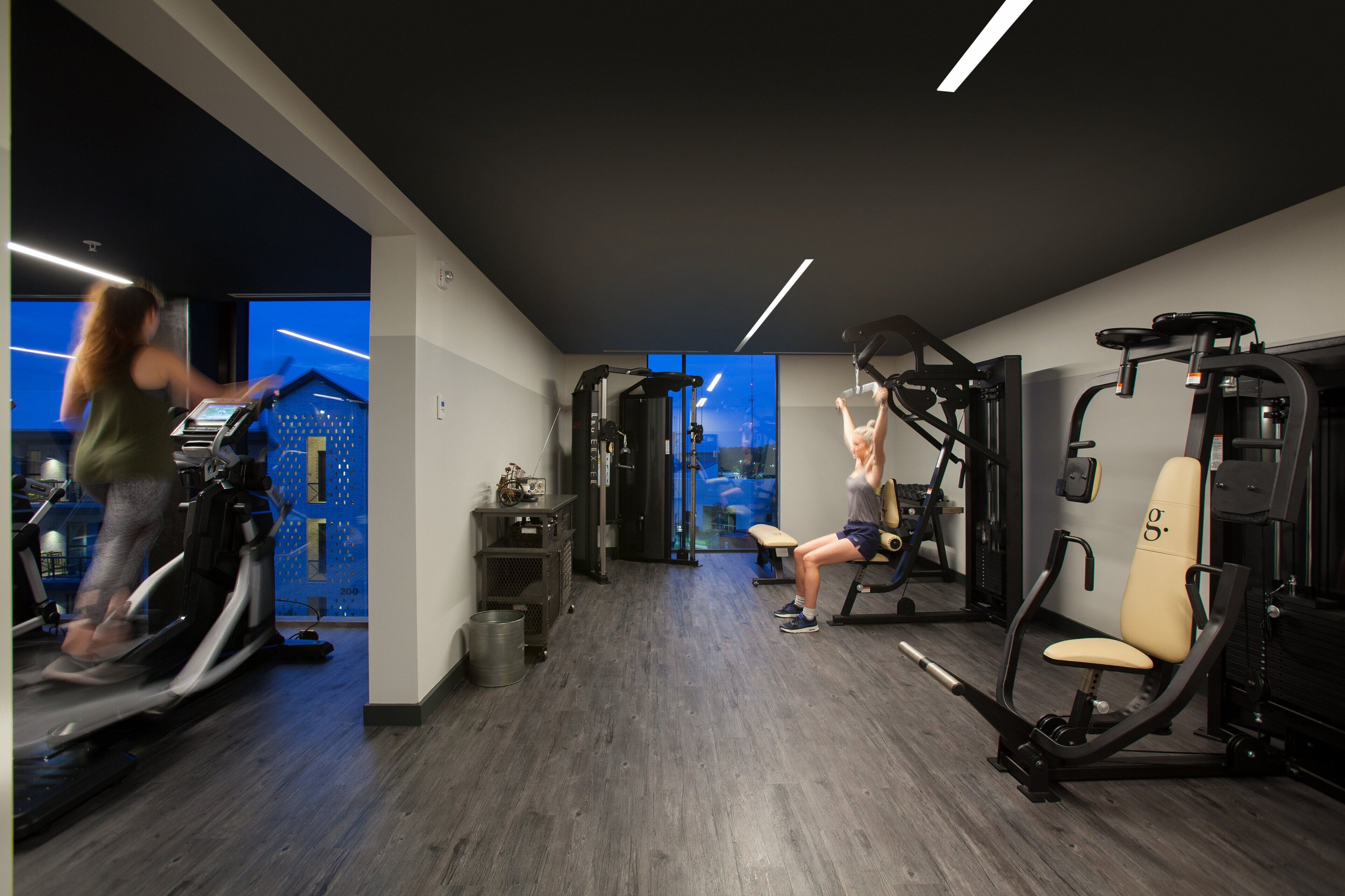 Een fitnessruimte met cardioapparaten, gewichten en een bank.