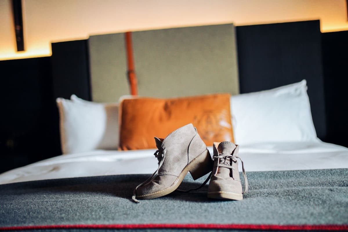 A bed with a grey carpet, two pillows, and a pair of shoes on the floor.