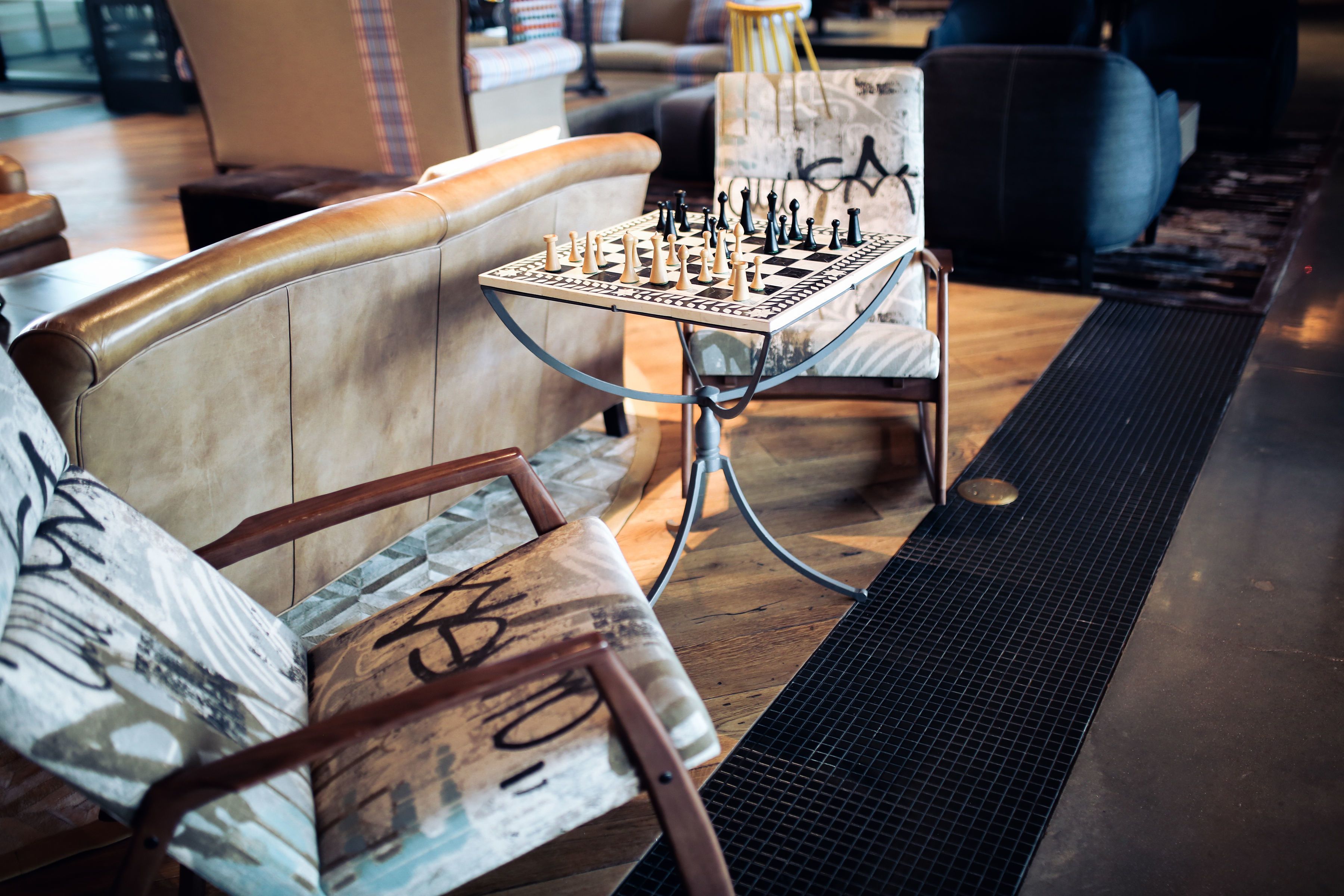 A chessboard on a metal table in a cozy seating area with a wooden floor and a patterned rug.
