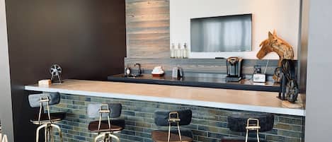 A modern kitchen with a bar area featuring four stools, a large mirror, and a mounted television.