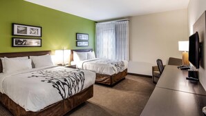 Ein Hotelzimmer mit zwei Betten, einem Schreibtisch, einem Fernseher und einem Fenster mit Vorhängen.