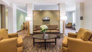 Eine Lobby mit einer Couch, zwei Sesseln, einem Couchtisch und einer Blumenvase.