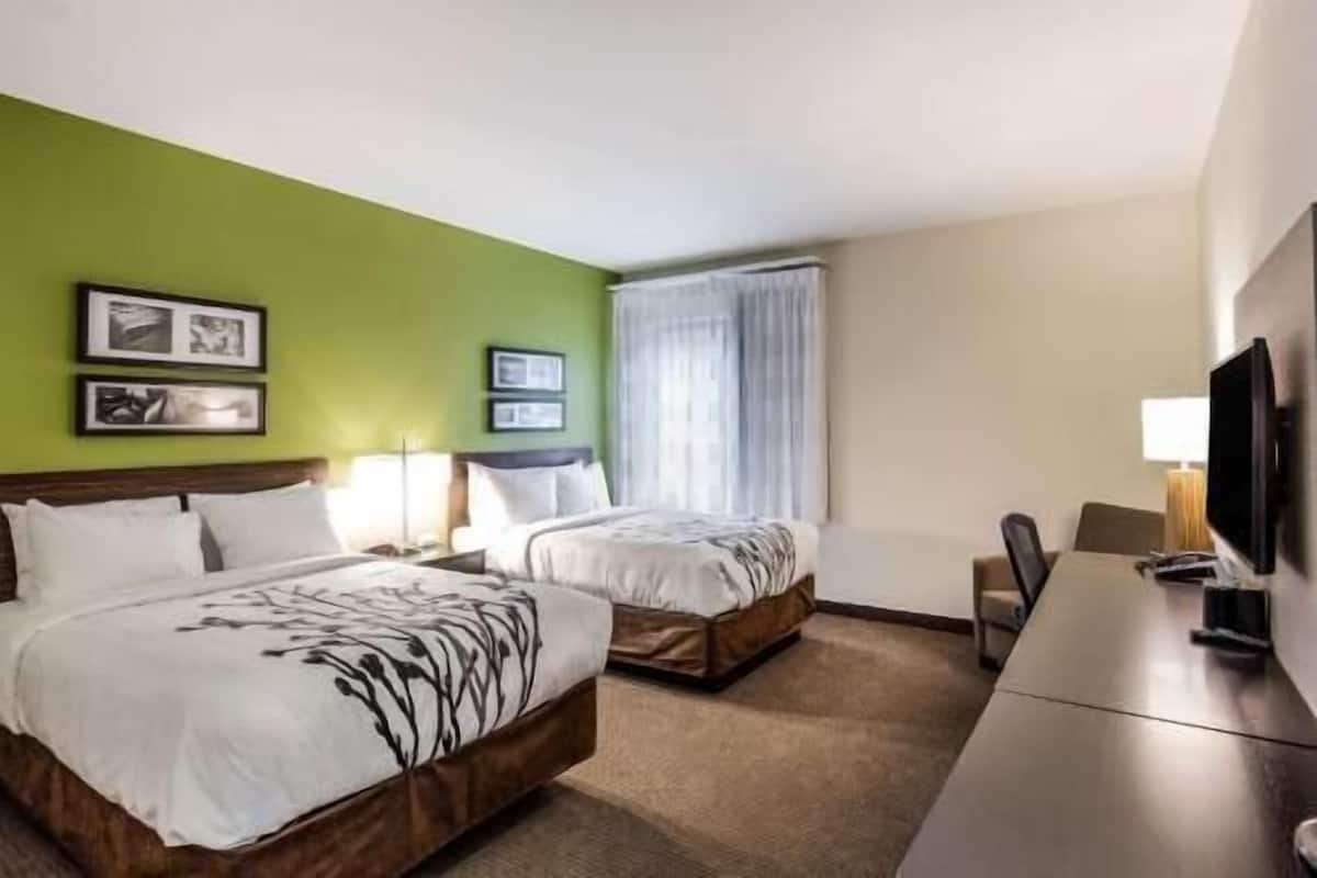 A hotel room with two beds, a desk, a television, and two framed pictures on the wall.