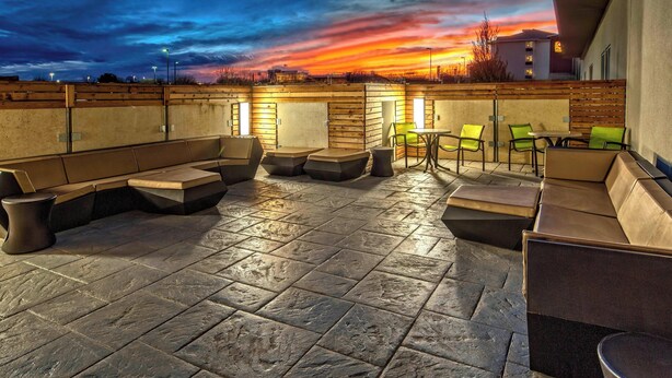 Un espace extérieur aménagé avec un sol en pierre, des bancs rembourrés et des chaises vertes.