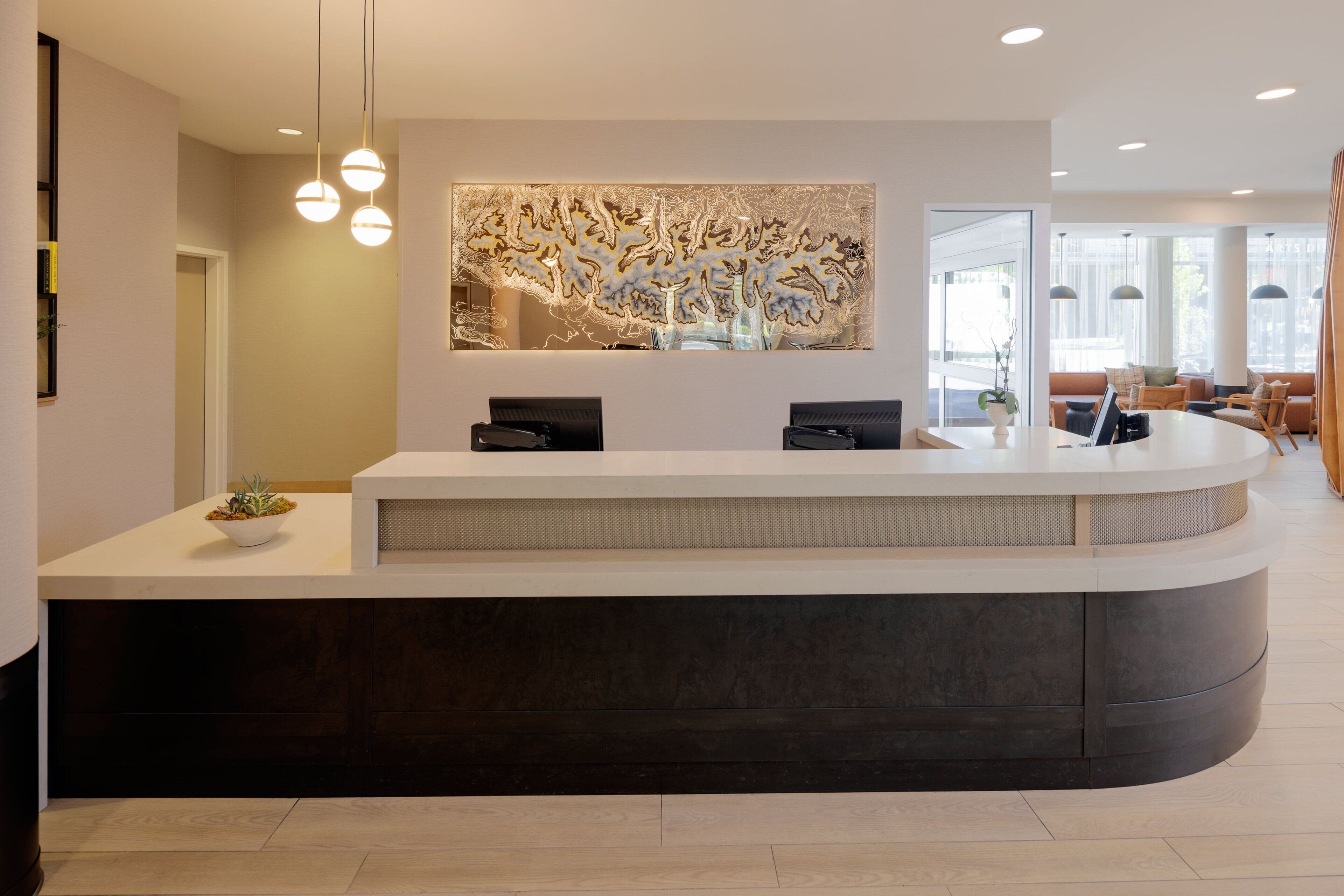 A reception desk with a modern design, a large abstract wall art piece above it, and a seating area with sofas and a coffee table in the background.