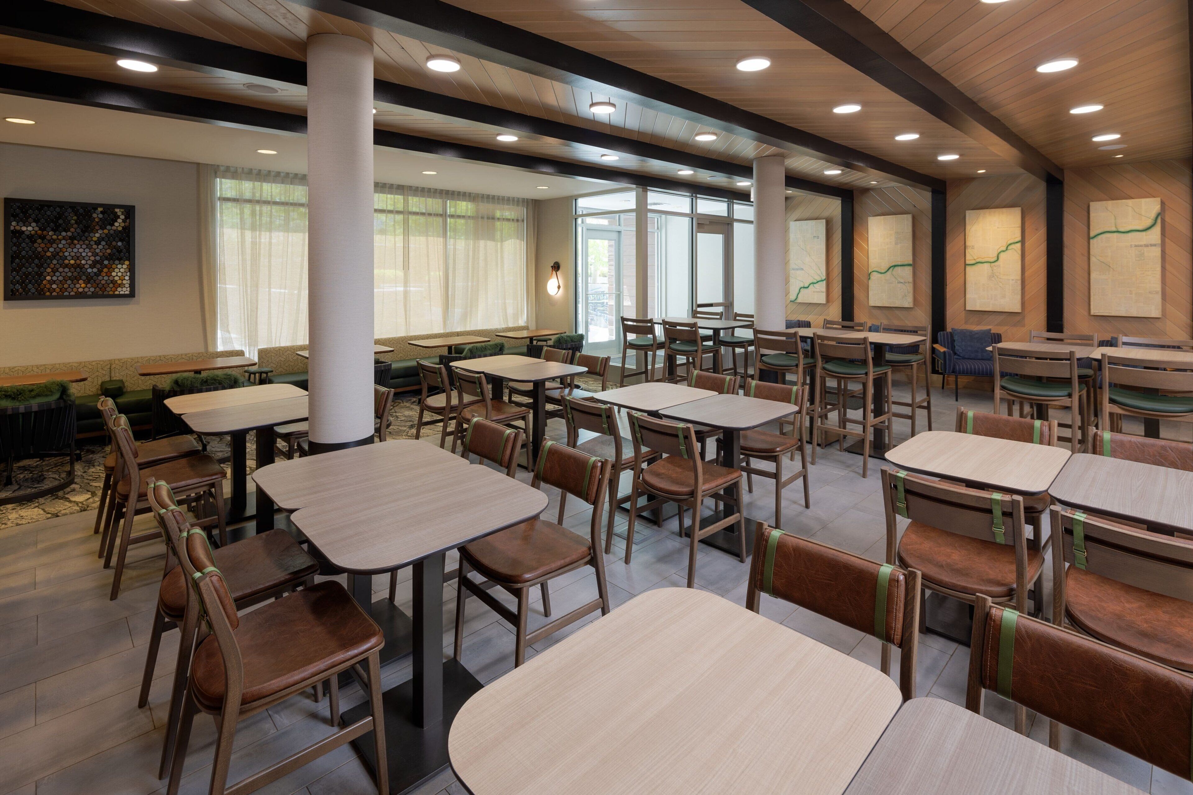 Een ruime eetruimte met meerdere tafels en stoelen, grote ramen met lichte gordijnen, en een modern plafondontwerp.