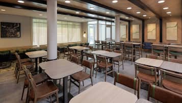Un comedor amplio con varias mesas y sillas, ventanas grandes con cortinas translúcidas y un diseño moderno en el techo.