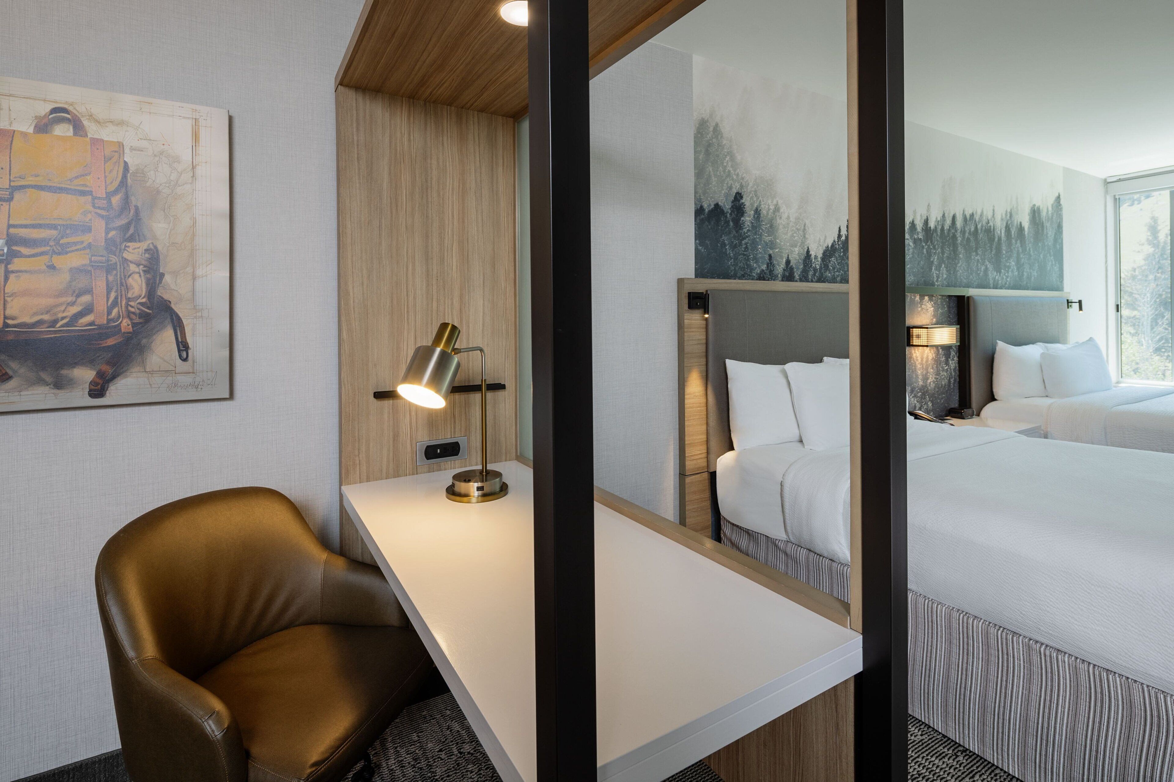 A hotel room with a wooden desk, a leather chair, a bed with white bedding, and a large mirror reflecting the room.
