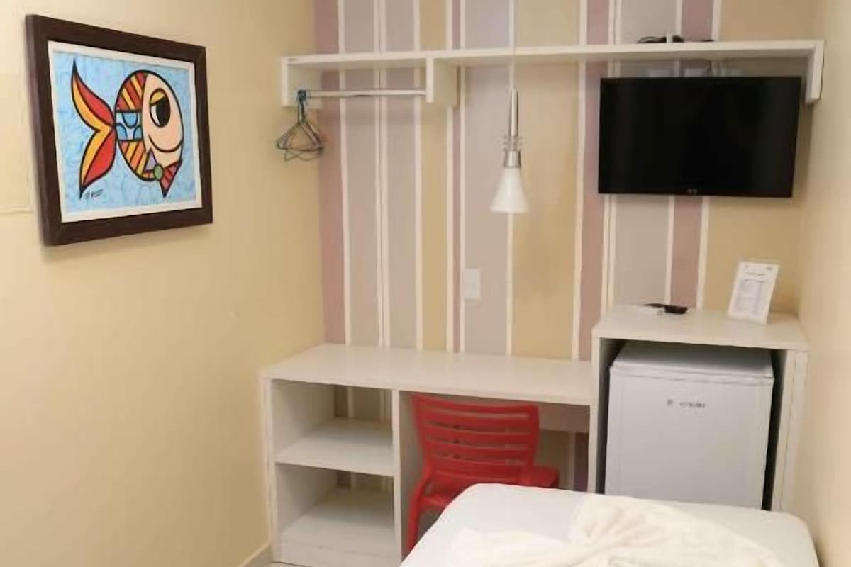 A hotel room with a bed, a desk, a television, and a painting on the wall.